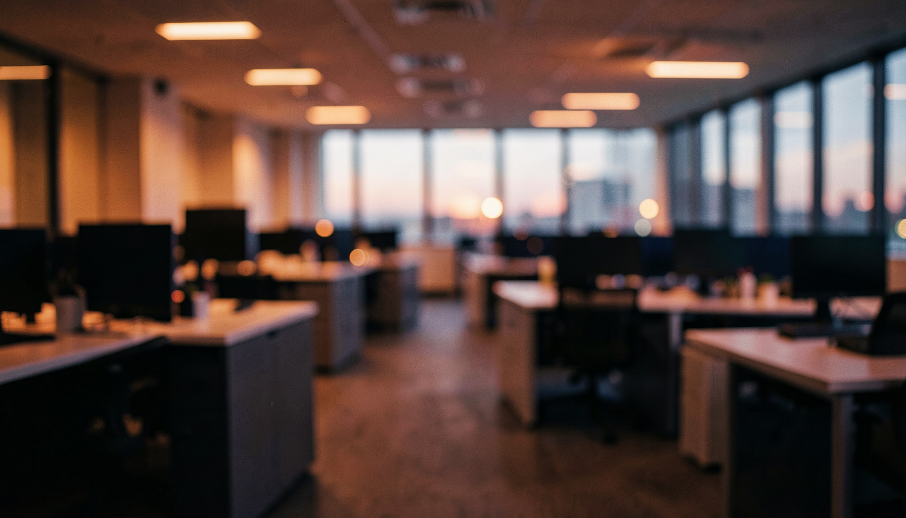 Wide cinematic frame of a softly lit modern office interior at dusk, warm amber and deep navy tones, shallow depth of field, conveying a calm professional workplace